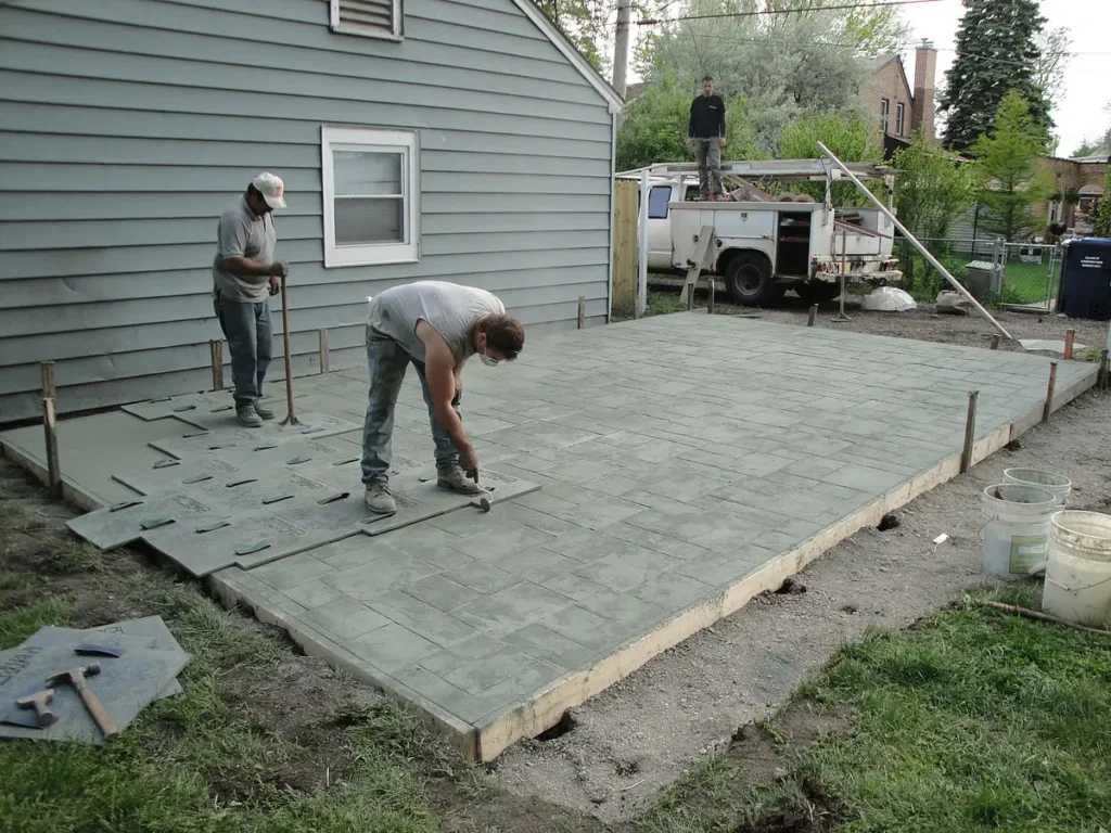 A Northland Concrete Services team member using a stamping tool to press a decorative pattern into fresh stamped concrete.